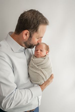 A tender moment as a parent gently cradles a swaddled newborn baby against a white background in a photo series.