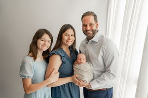 Family members pose together in a bright studio space wearing coordinated gray and navy outfits.