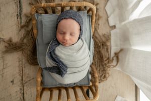 Overhead view of a sleeping baby wrapped in gray swaddling cloth lying in a rustic wooden basket.
