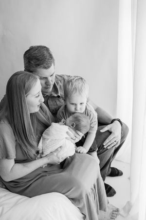 An intimate family moment captured in black and white with parents cuddling their young child on a couch.