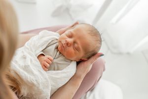 Sleeping newborn baby in white wrap against soft white background.