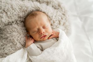 Peaceful sleeping newborn baby wearing white on soft grey blanket in natural light.