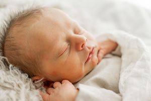 Peaceful sleeping newborn baby in white linen wrap.
