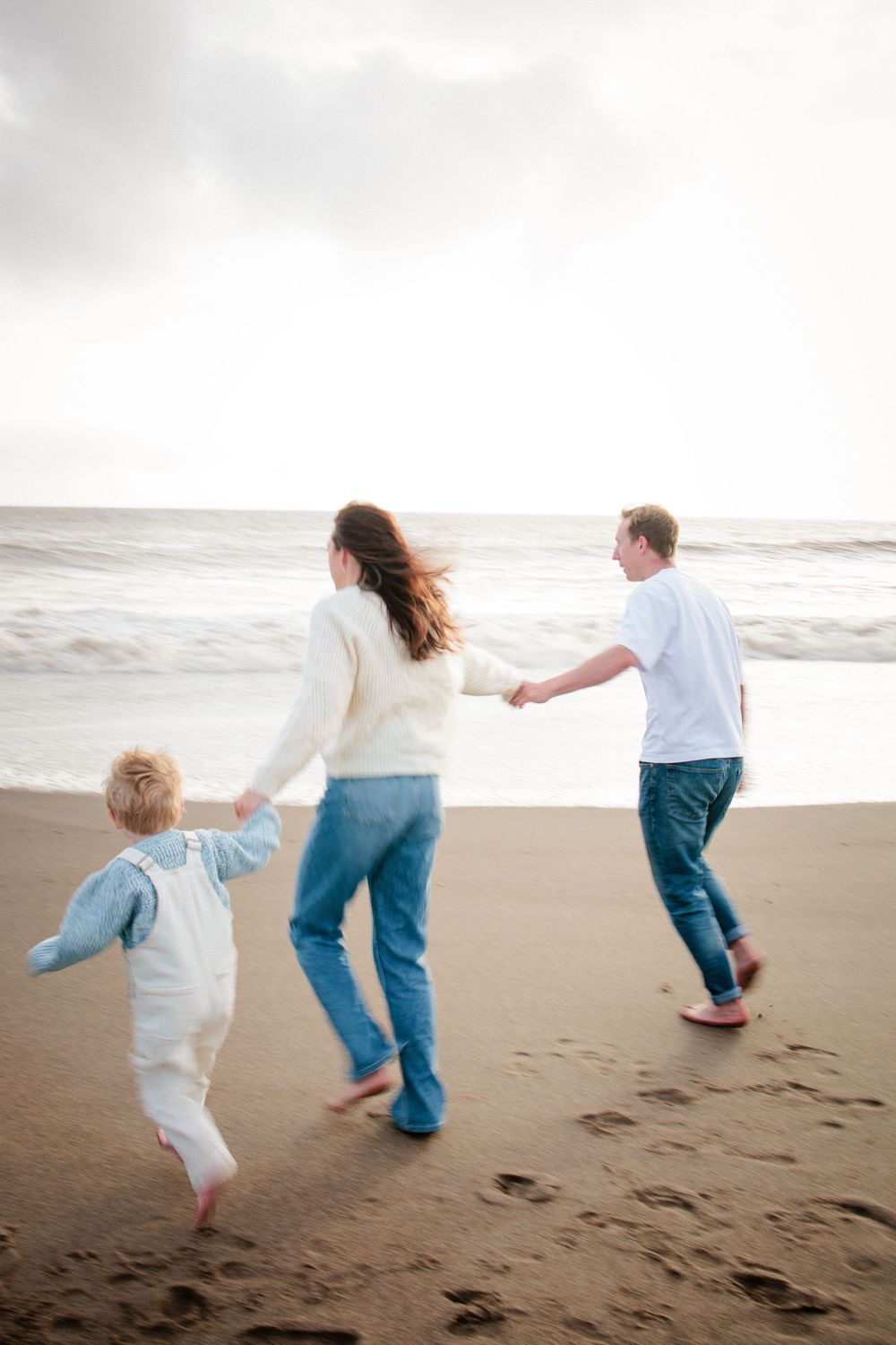 Happy family holding hands and running together along a sandy beach toward the ocean waves.