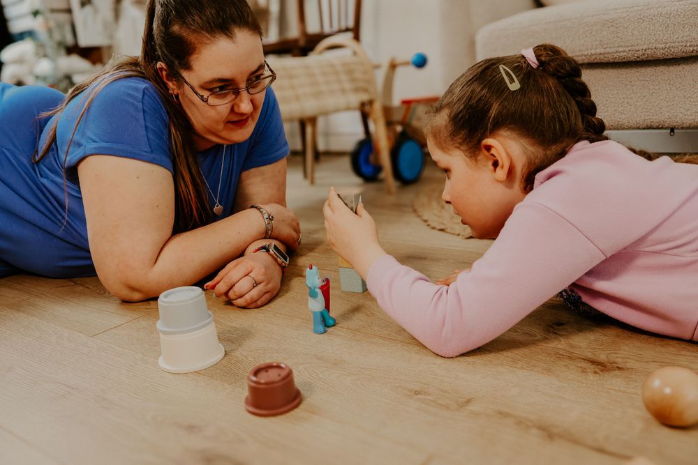 Woman and young girl lying on floor playing with small toys and cups together.