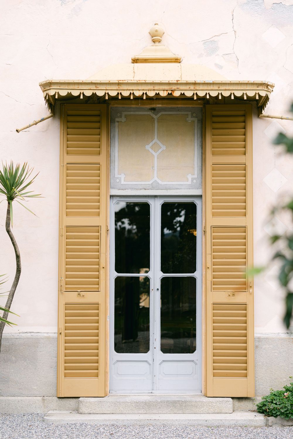Elegant yellow shuttered doorway with ornate white trim and glass panels in Mediterranean style.