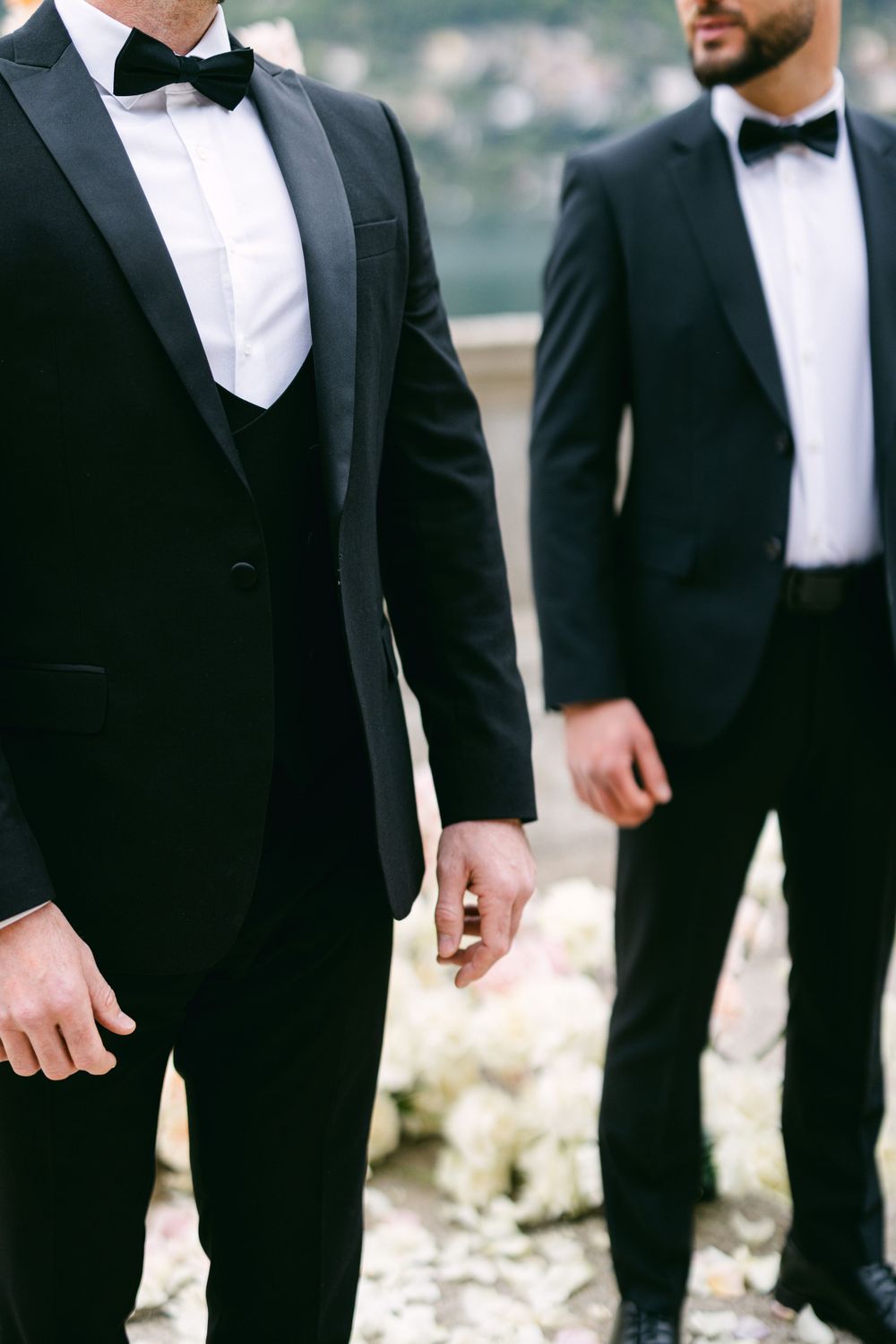 Two men in classic black tuxedos and bow ties stand together at formal event.