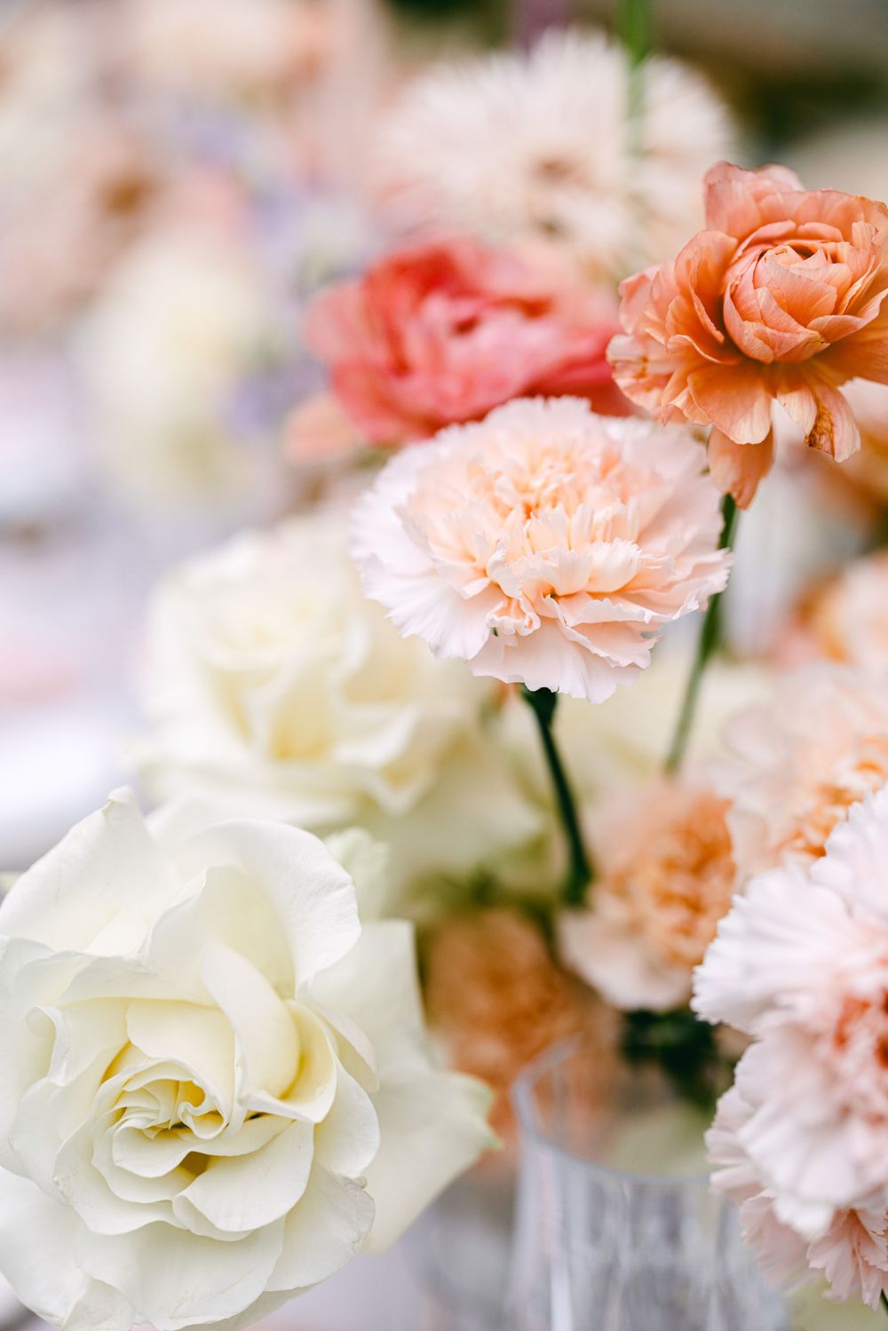 Delicate arrangement of peach and white roses and carnations in soft focus.