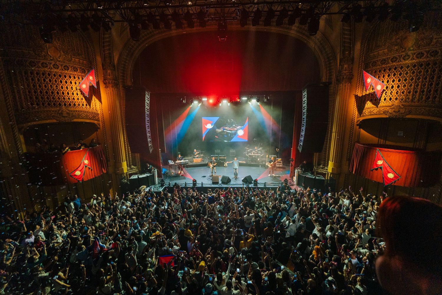 Packed historic theater venue with ornate architecture and vibrant stage lighting during live performance.
