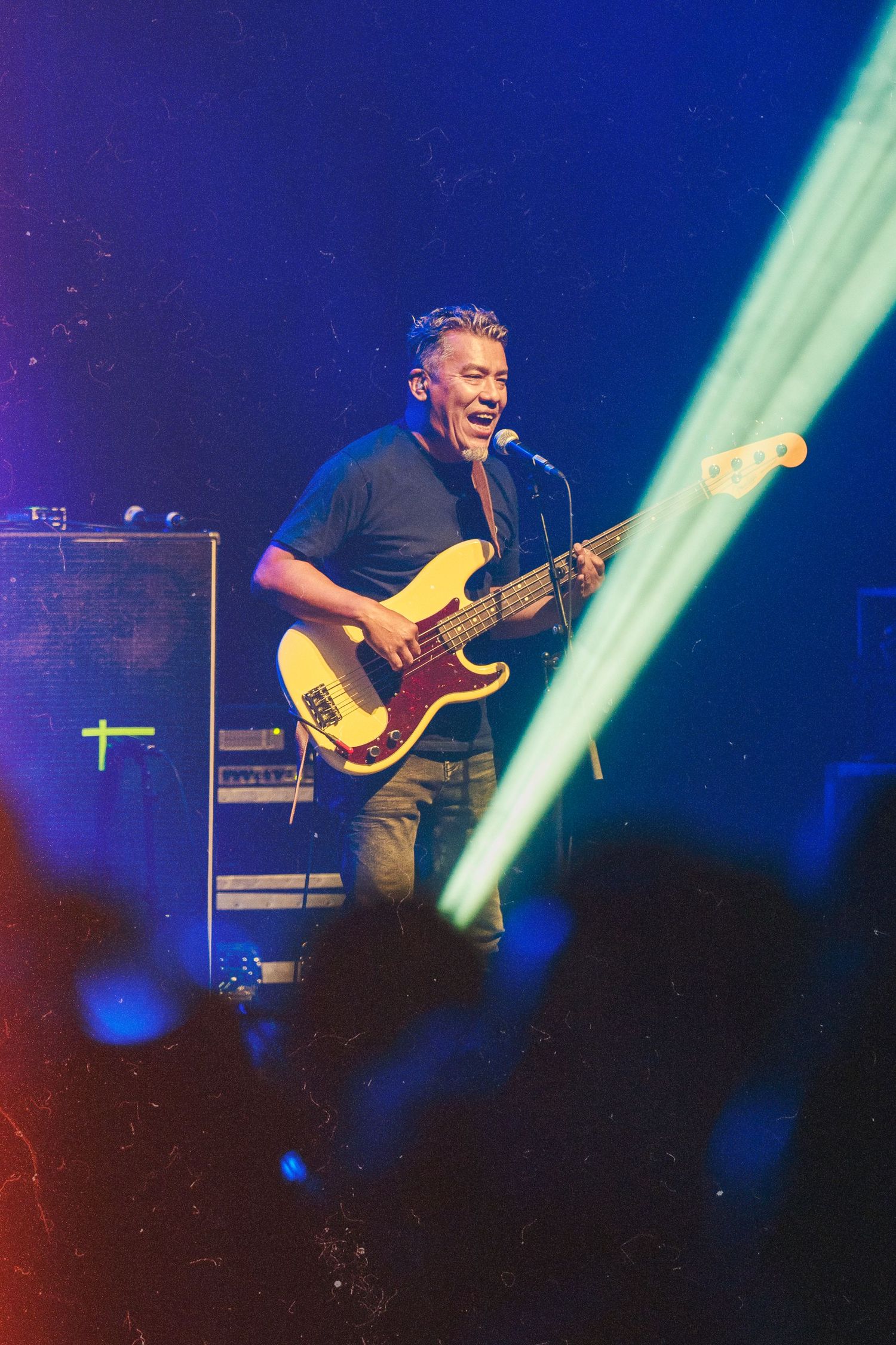 Bass guitarist performs energetically under blue stage lighting during concert.