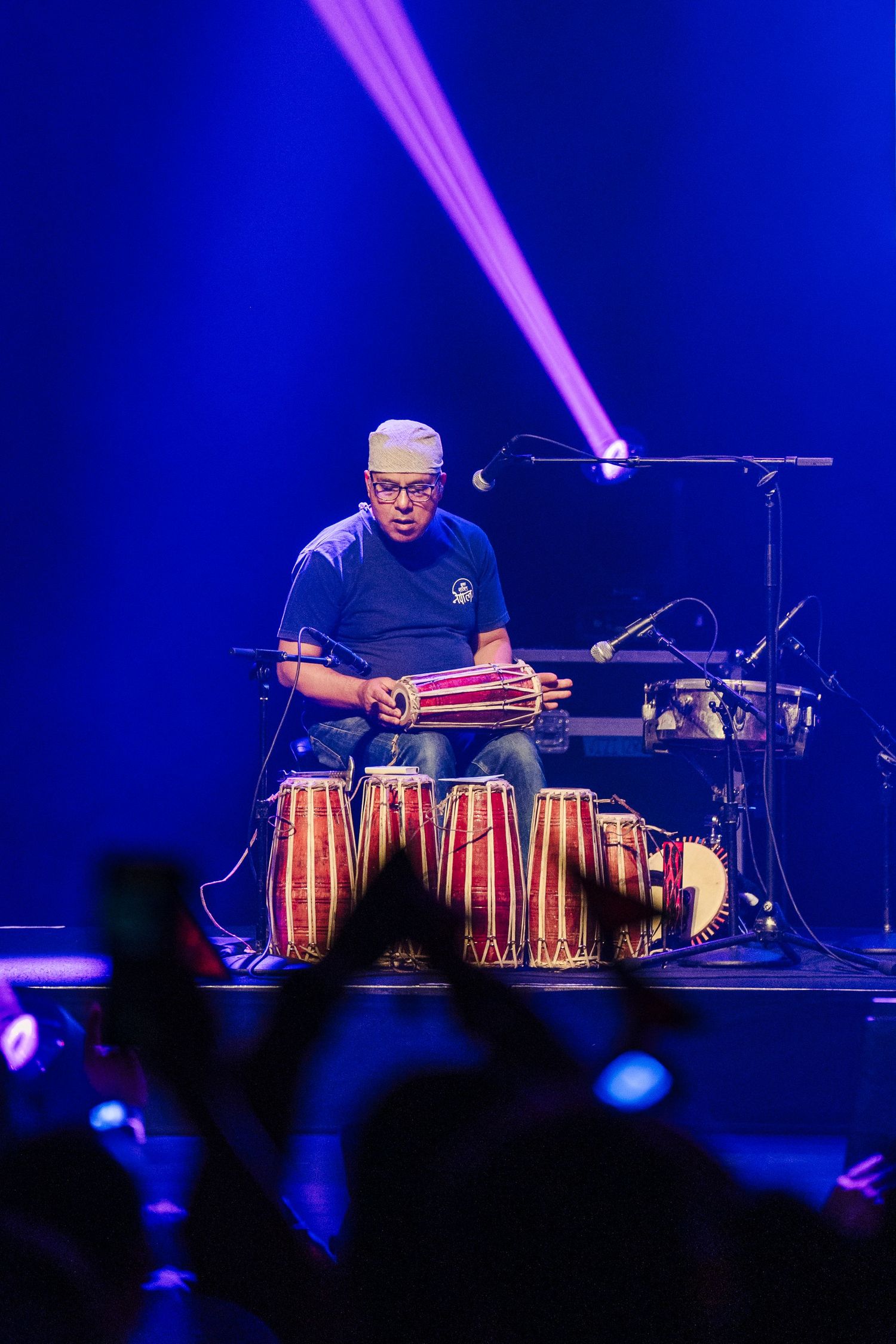 Percussionist plays traditional conga drums under purple stage lighting during live performance.