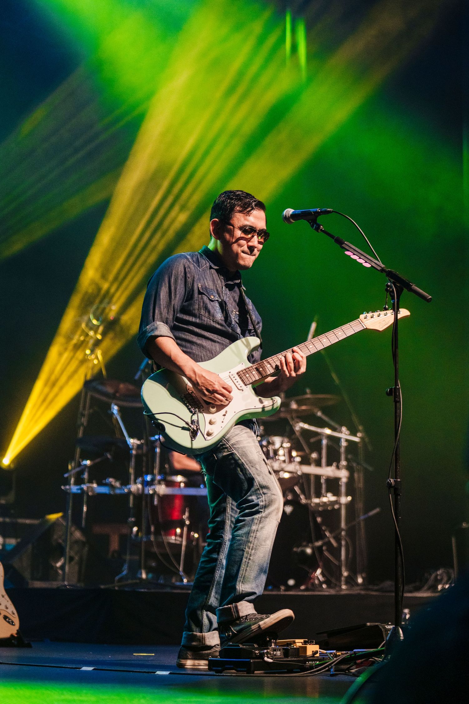 Guitarist performs on stage with bright yellow and green spotlights creating dramatic atmosphere.