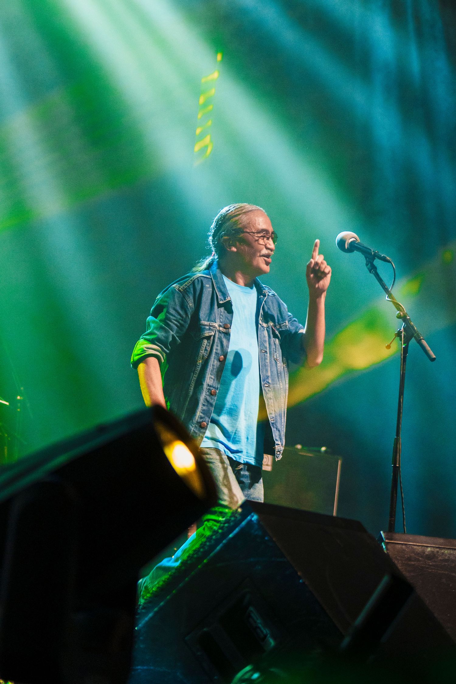 Performer points upward during passionate performance with dramatic green stage lighting.