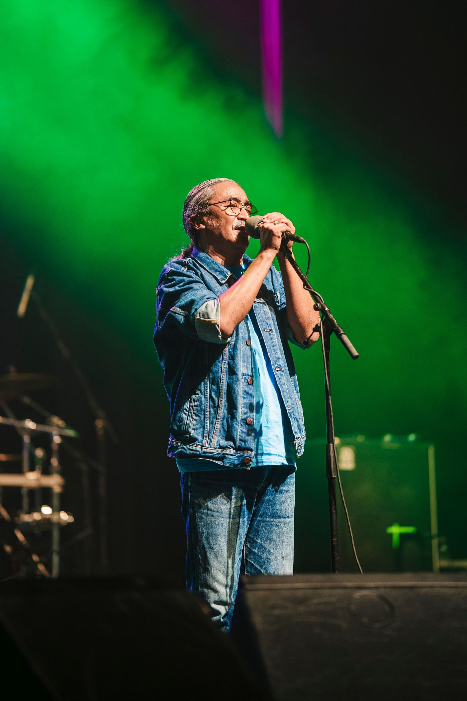 Lead singer performs passionately on stage with green lighting and jean jacket during live concert performance.