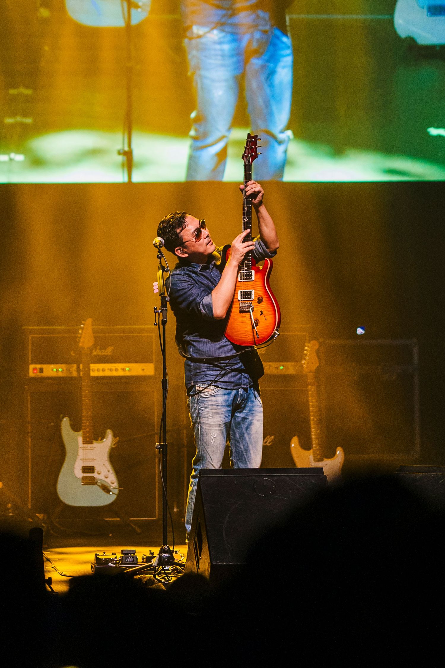 Musician performs passionately on stage with guitar under dramatic lighting.