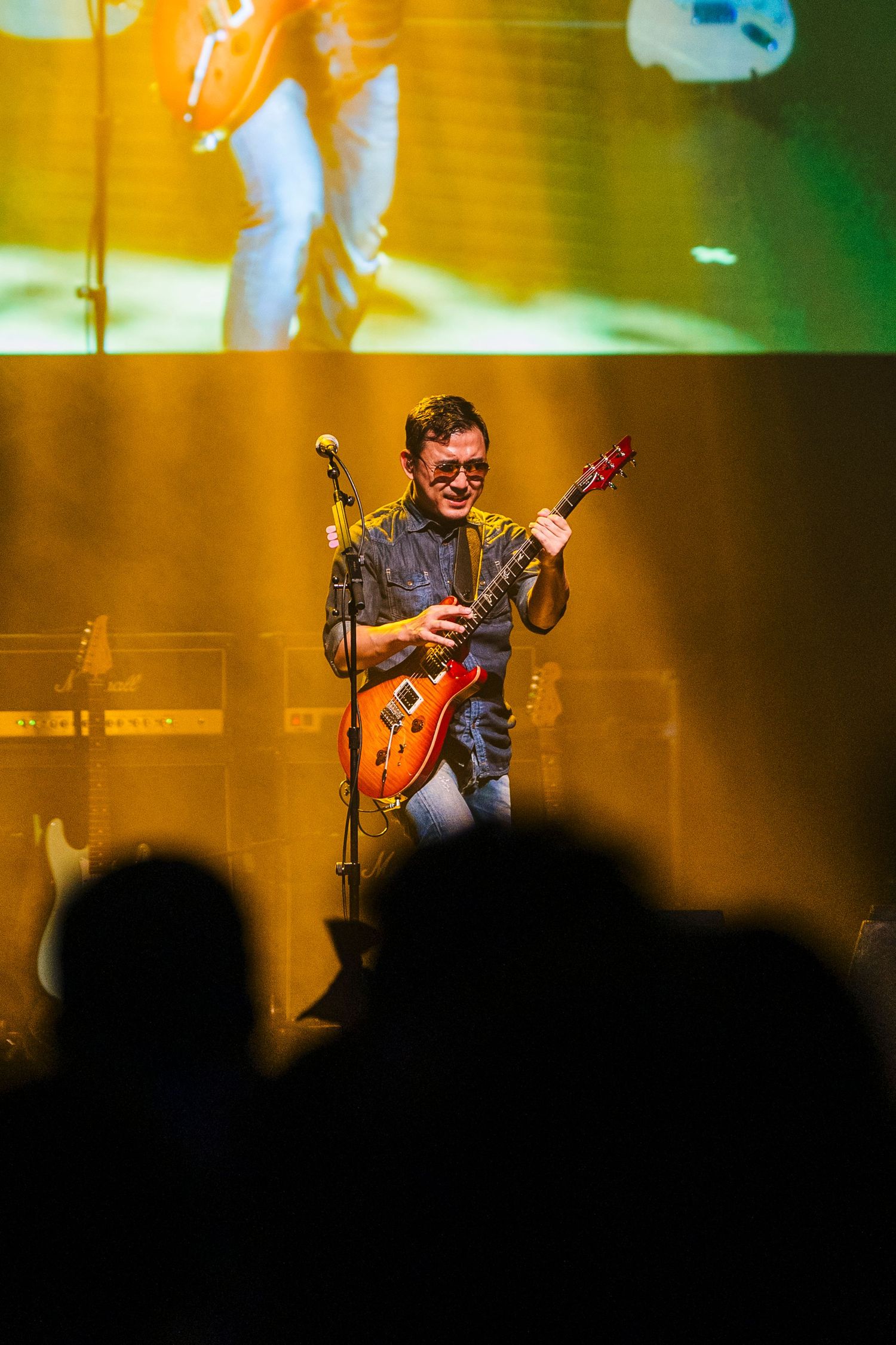 Guitarist performs on stage with orange Les Paul guitar under warm stage lighting.