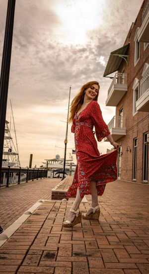 Woman in red dress twirls by marina boardwalk during golden sunset.