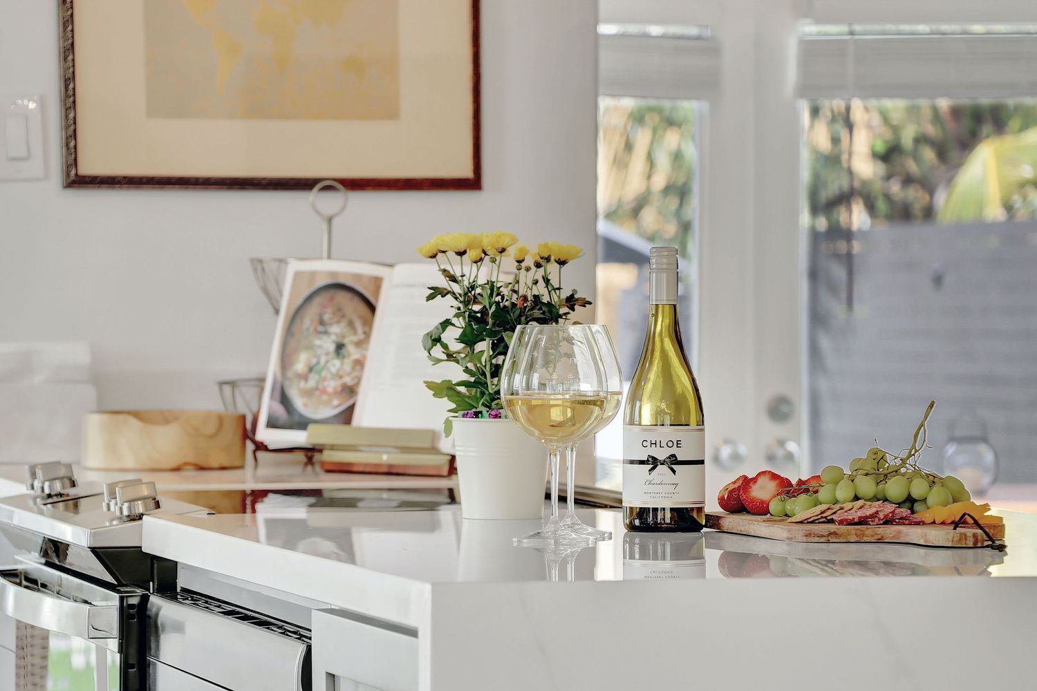 A light and airy room features a long table set for a gathering with elegant white plates and glassware.  All possible at Realty Frame.