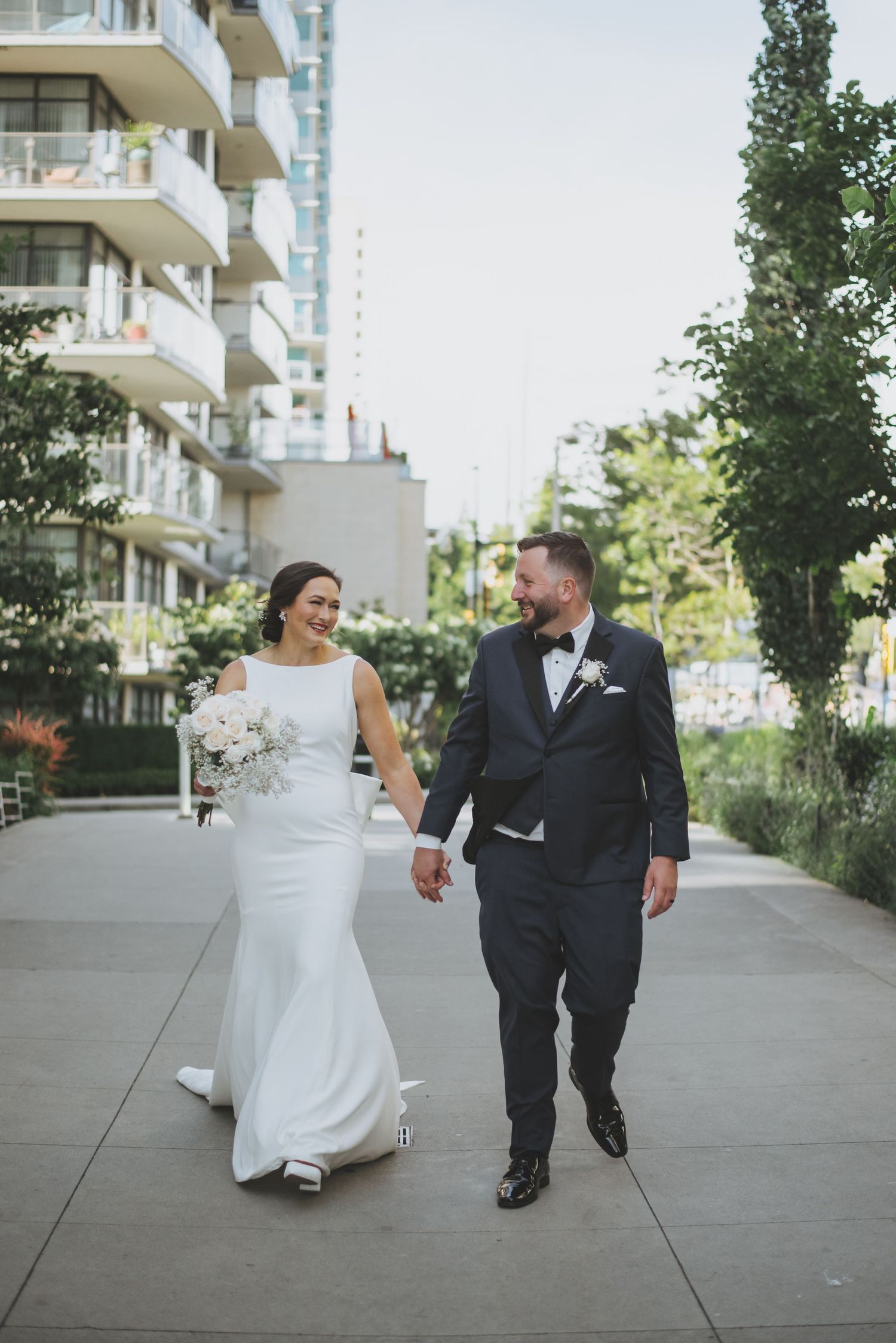 Couple walking hand in hand along urban pathway with modern apartment buildings behind them.