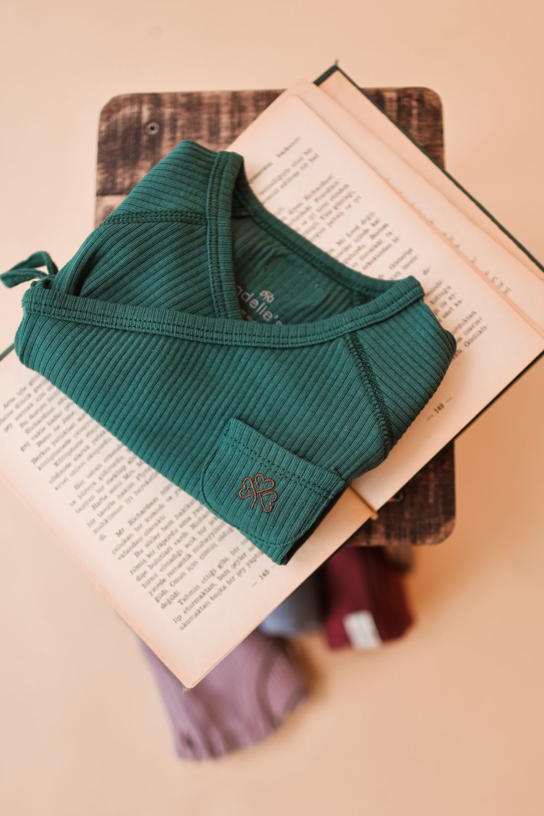 A green ribbed tank top rests on an open book against a wooden backdrop.
