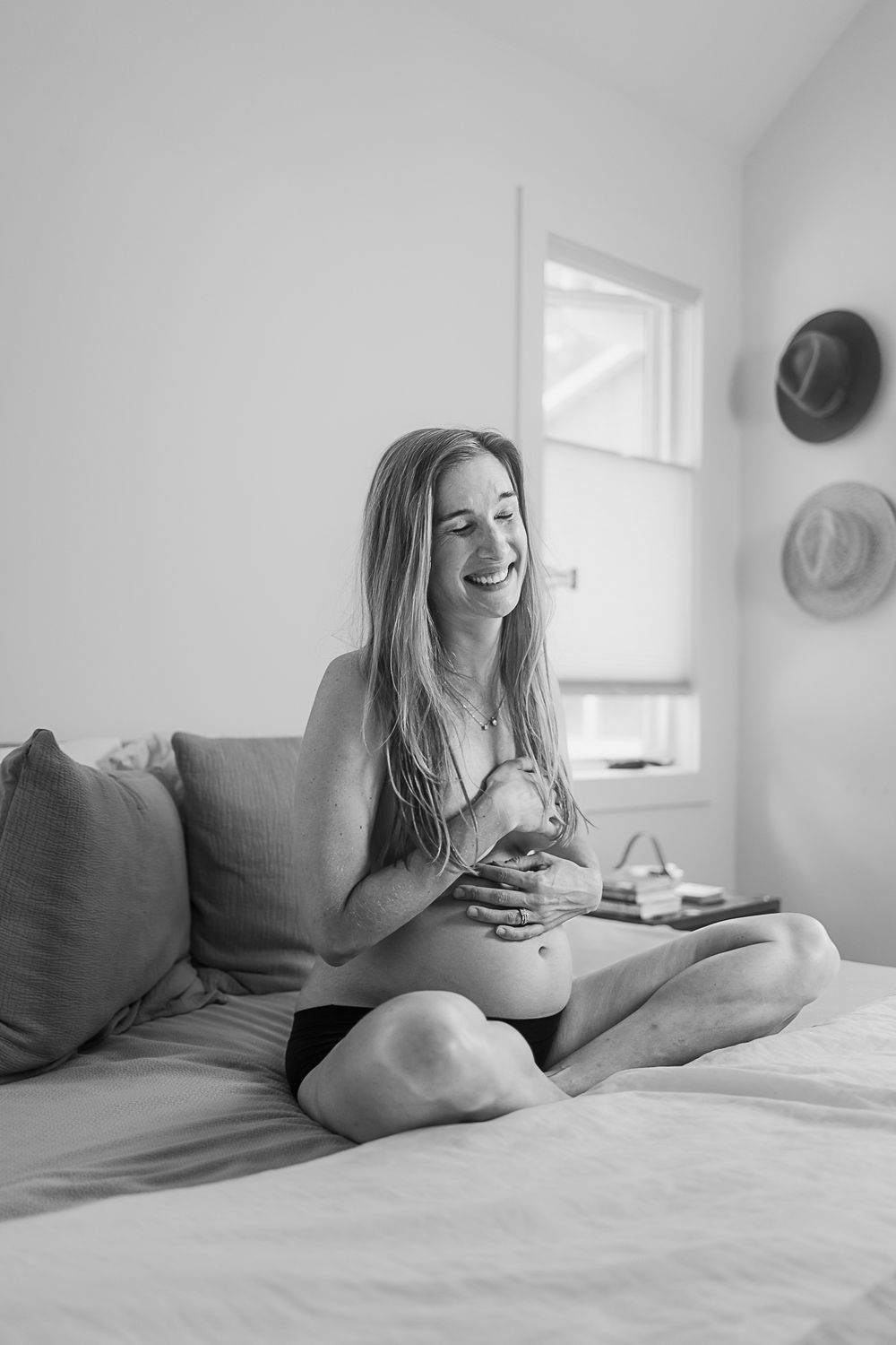 A candid black and white maternity moment captured on a comfortable bed.