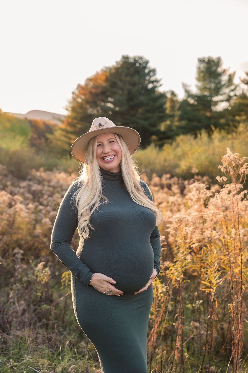 Maternity photo session in a golden autumn field at sunset with tall grass and warm lighting.