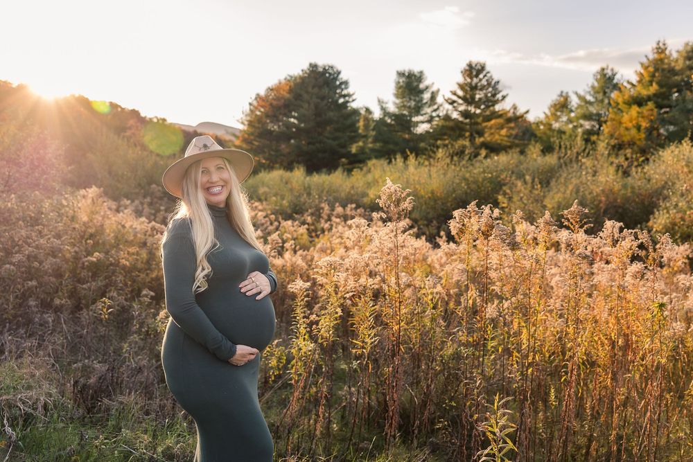 Golden sunlight illuminates a field of tall autumn grasses at sunset during a maternity photography session.