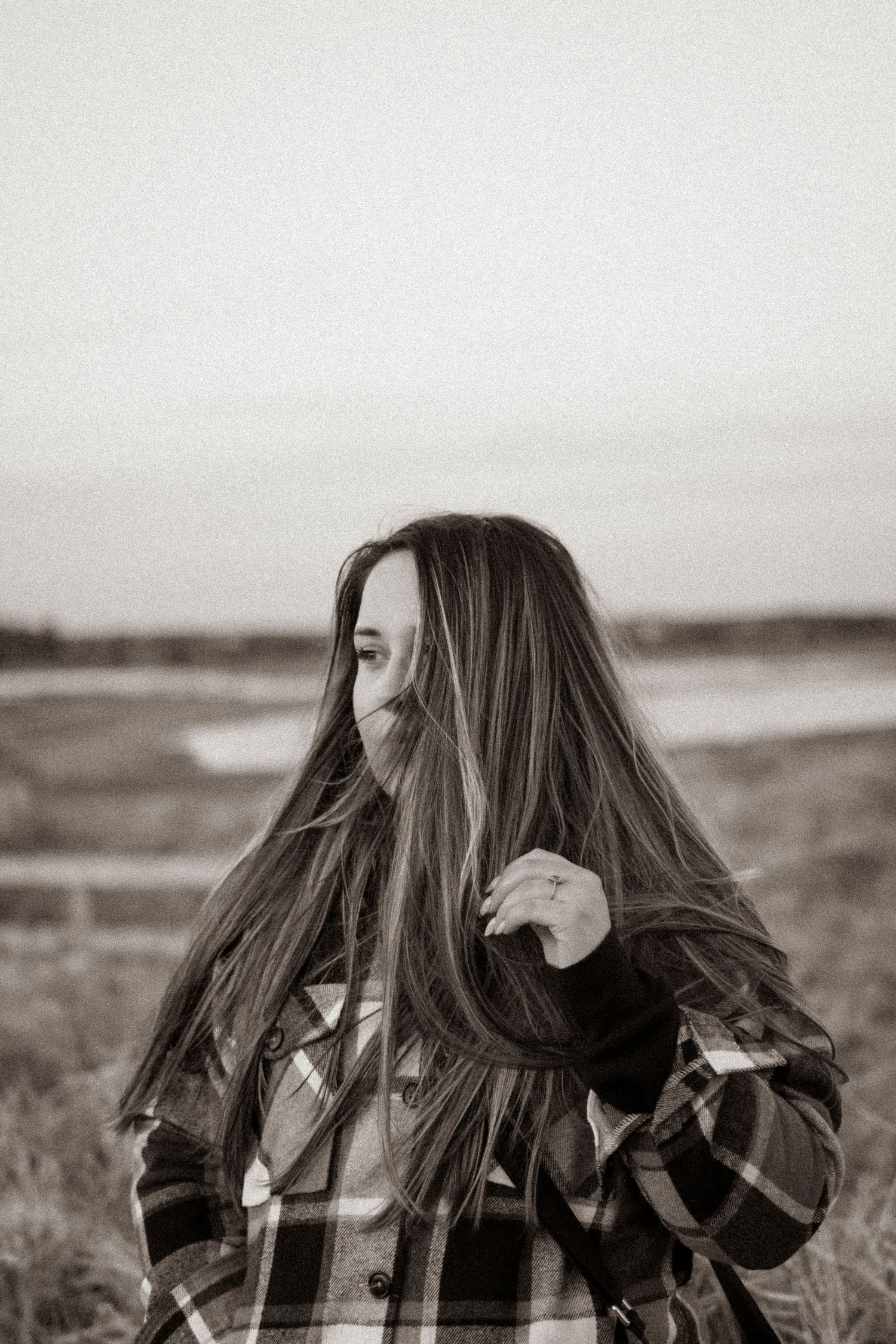 black and white Image of a woman at the beach with windswept hair across her face.