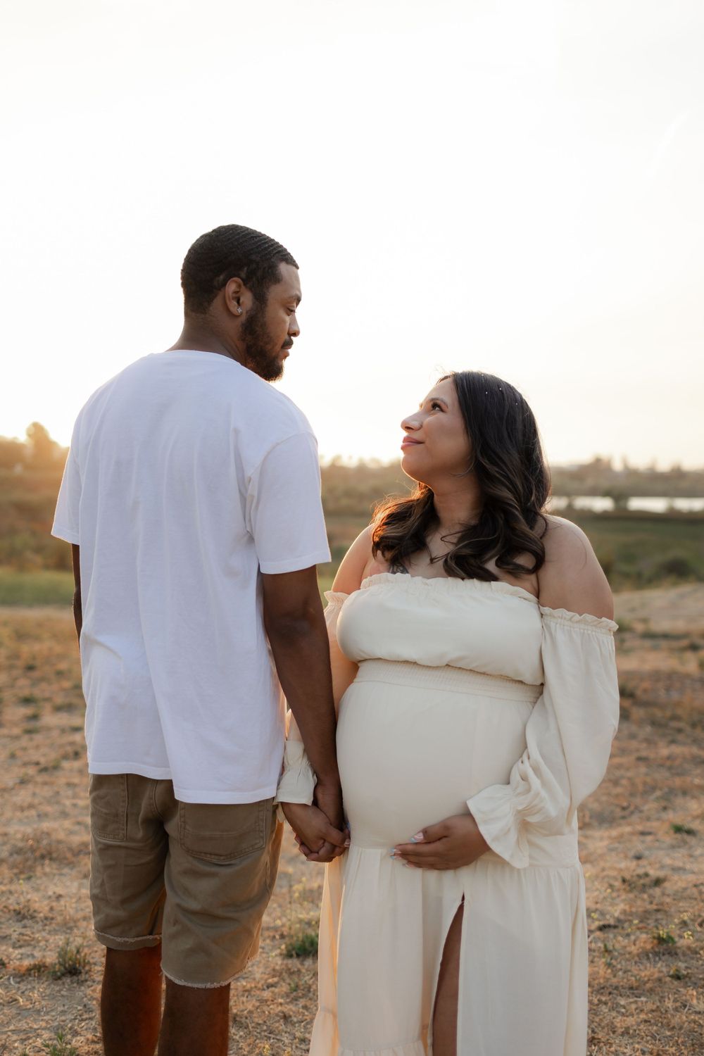 A couple holds hands during a sunset maternity photoshoot in an outdoor setting.
