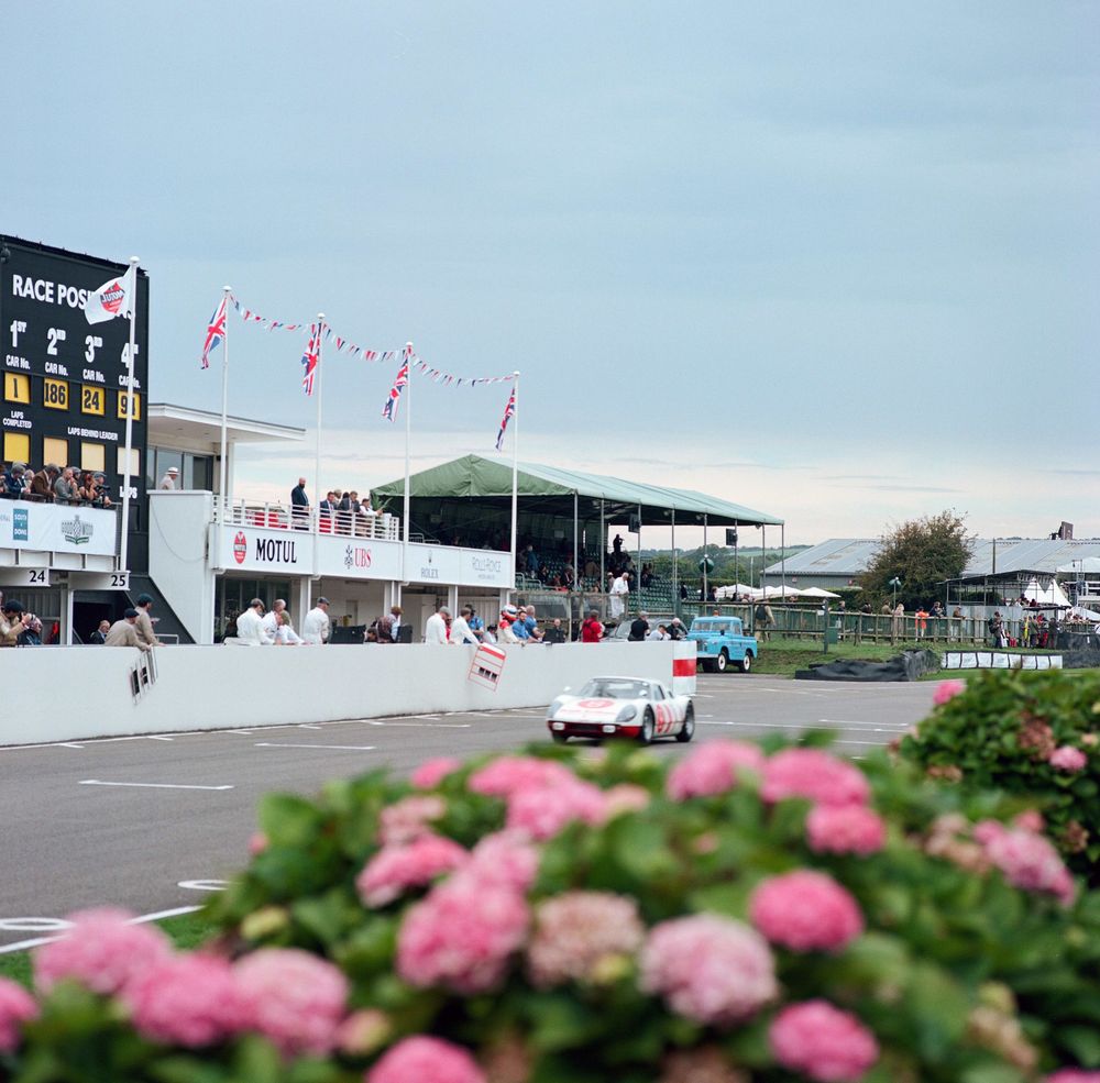 Vintage White and Red Porsche Racecar driving on Goodwood Track during Goodwood Revival. Part of Team Ikuzawa's display in 2024.