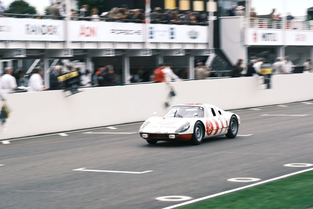 Vintage White and Red Porsche Racecar driving on Goodwood Track during Goodwood Revival. Part of Team Ikuzawa's display in 2024.