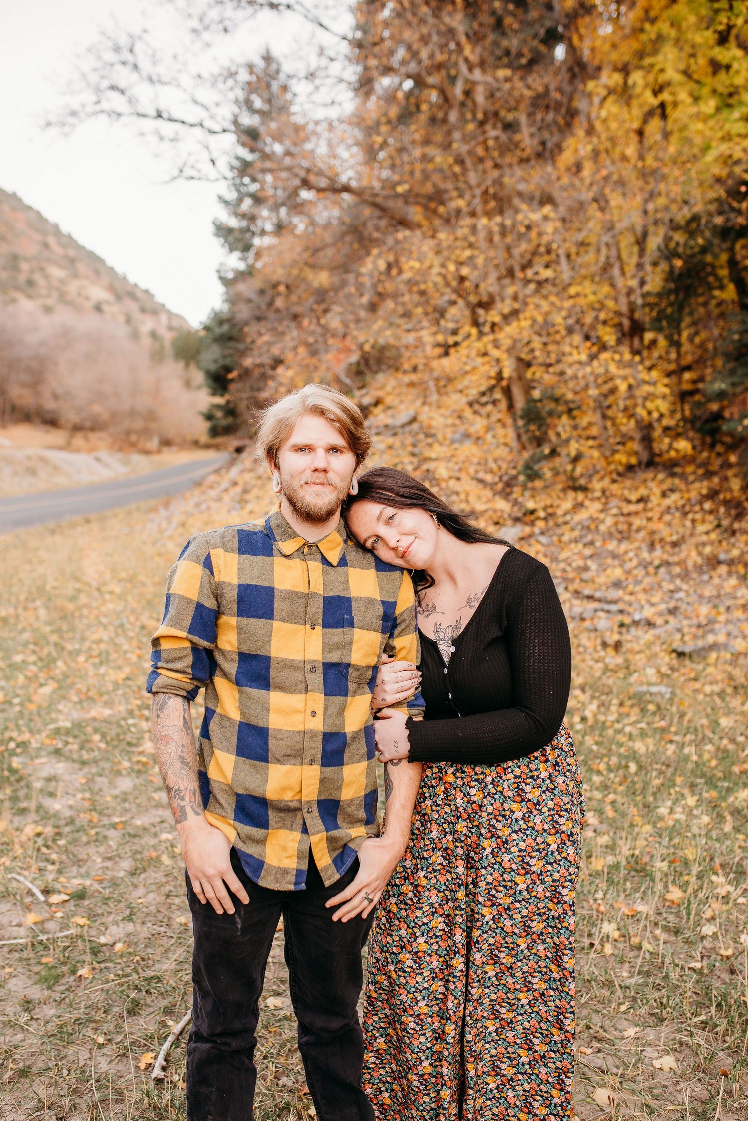 A couple embraces on a winding mountain road surrounded by fall foliage.