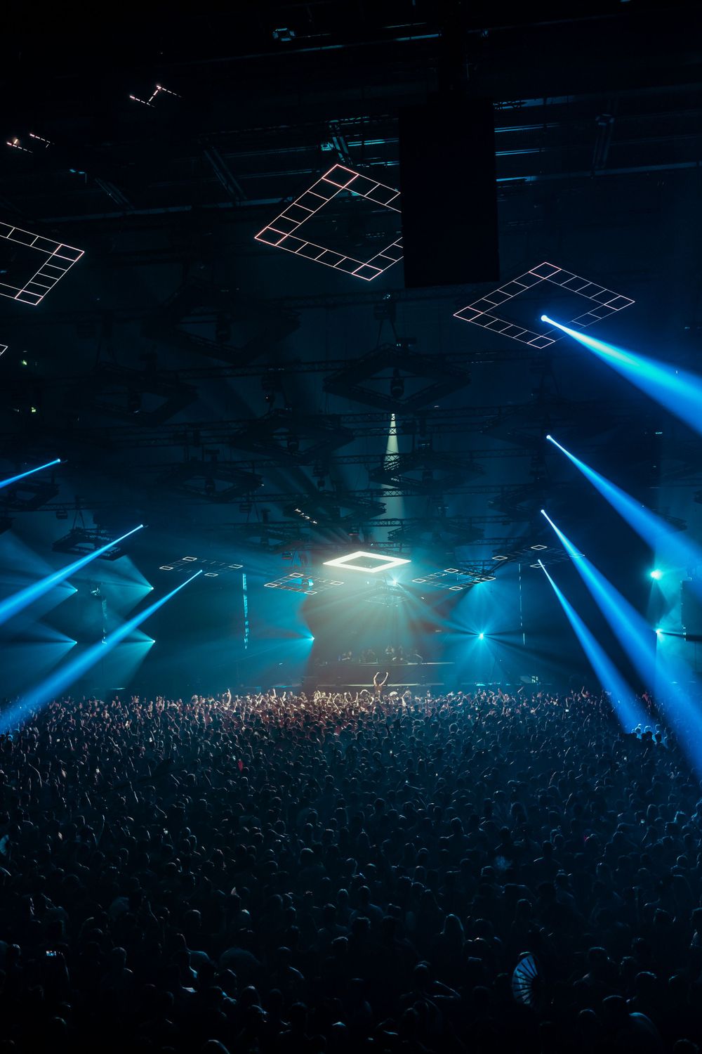 Massive concert venue with geometric lighting design above crowd silhouettes.
