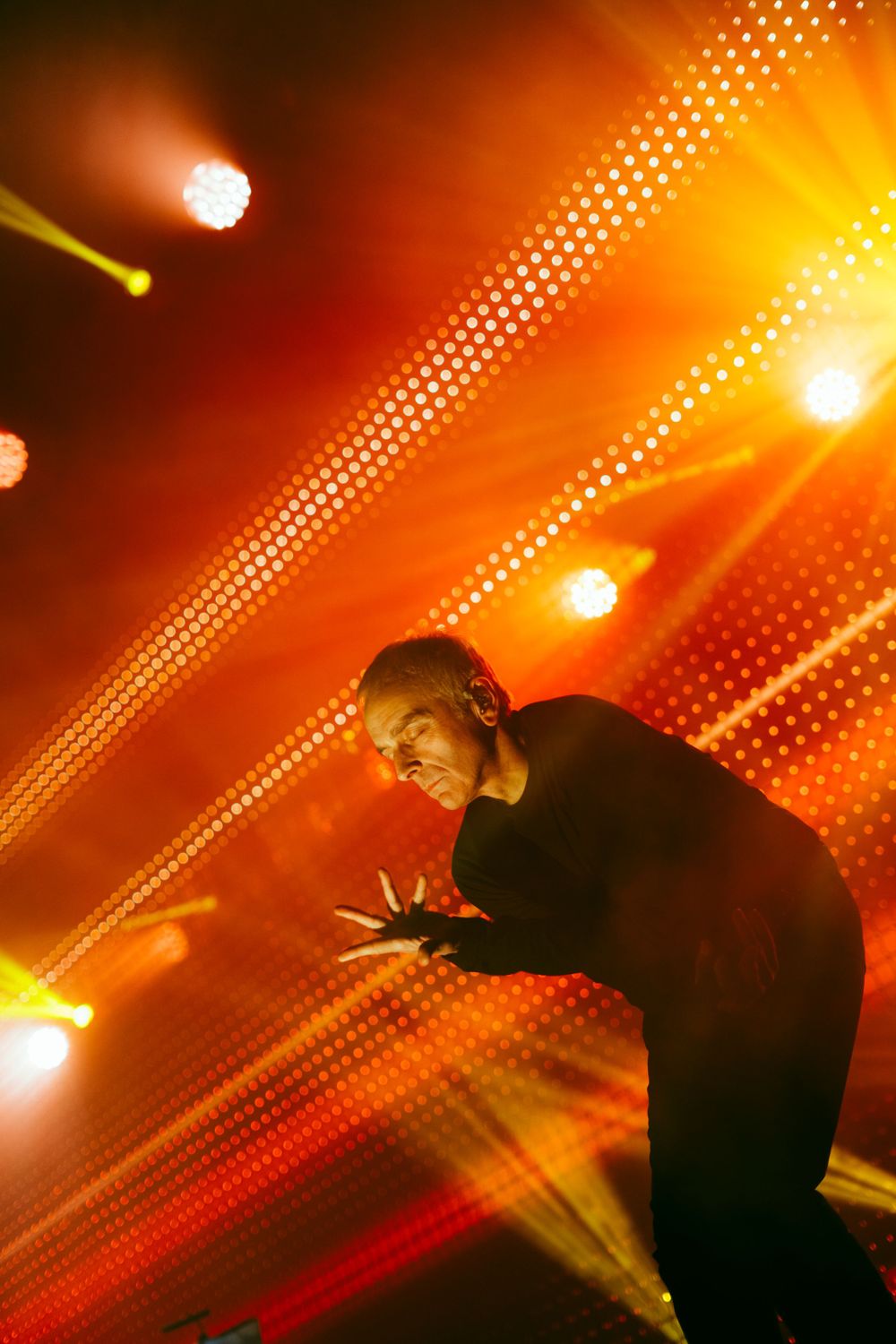 Silhouetted figure performs against vibrant orange stage lighting and effects.
