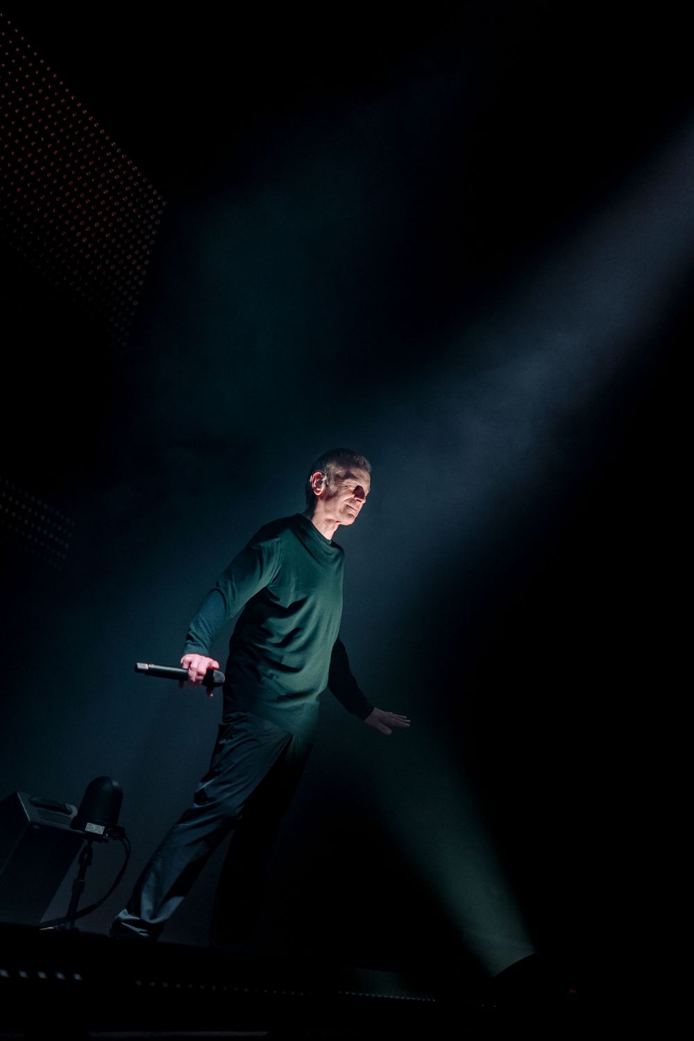 Performer moves dramatically across dark stage with blue spotlight.