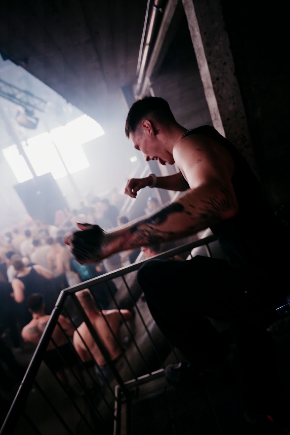 DJ performing in dark nightclub setting with dramatic backlighting and crowd silhouettes.
