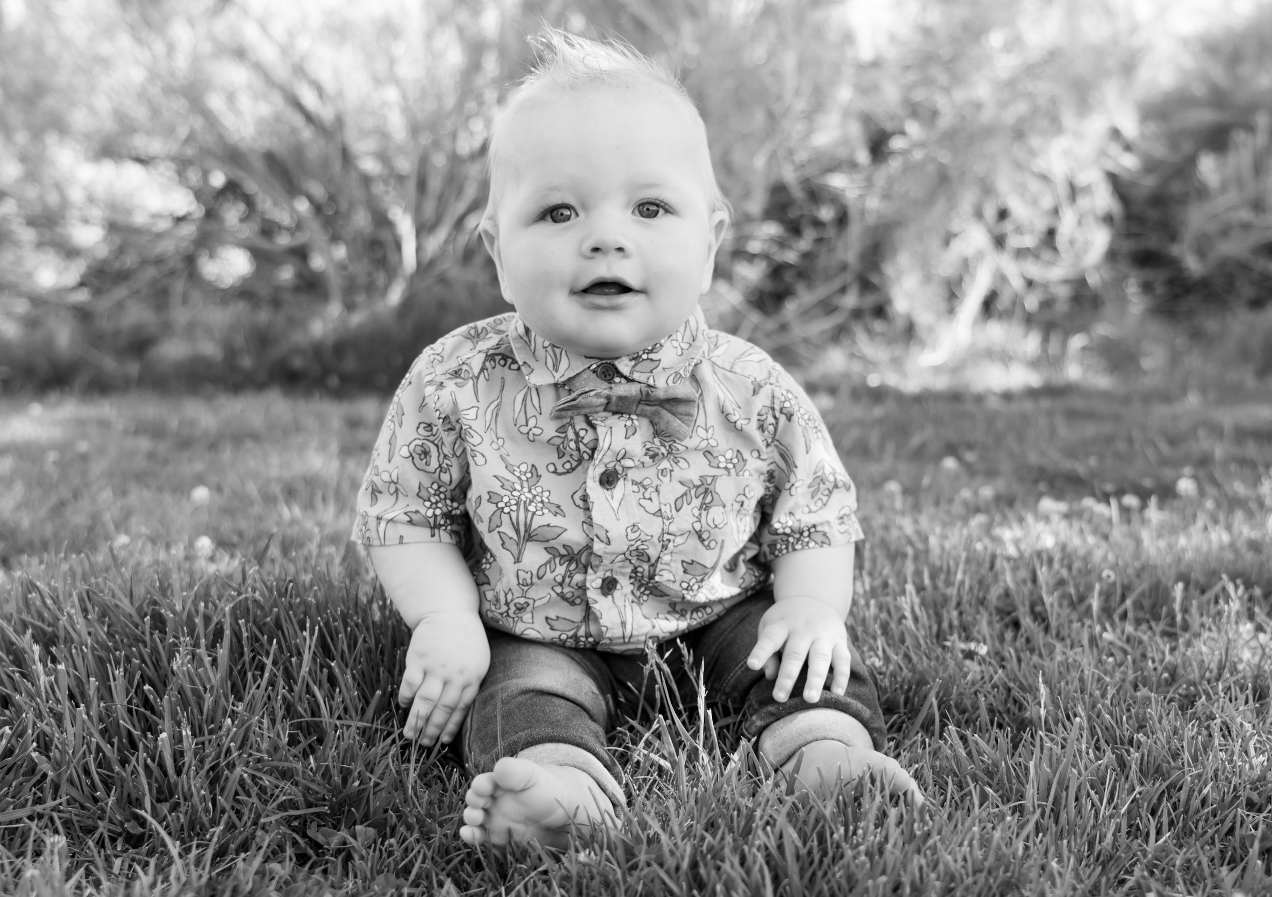 Baby in floral shirt sitting on grass in black and white portrait photography.