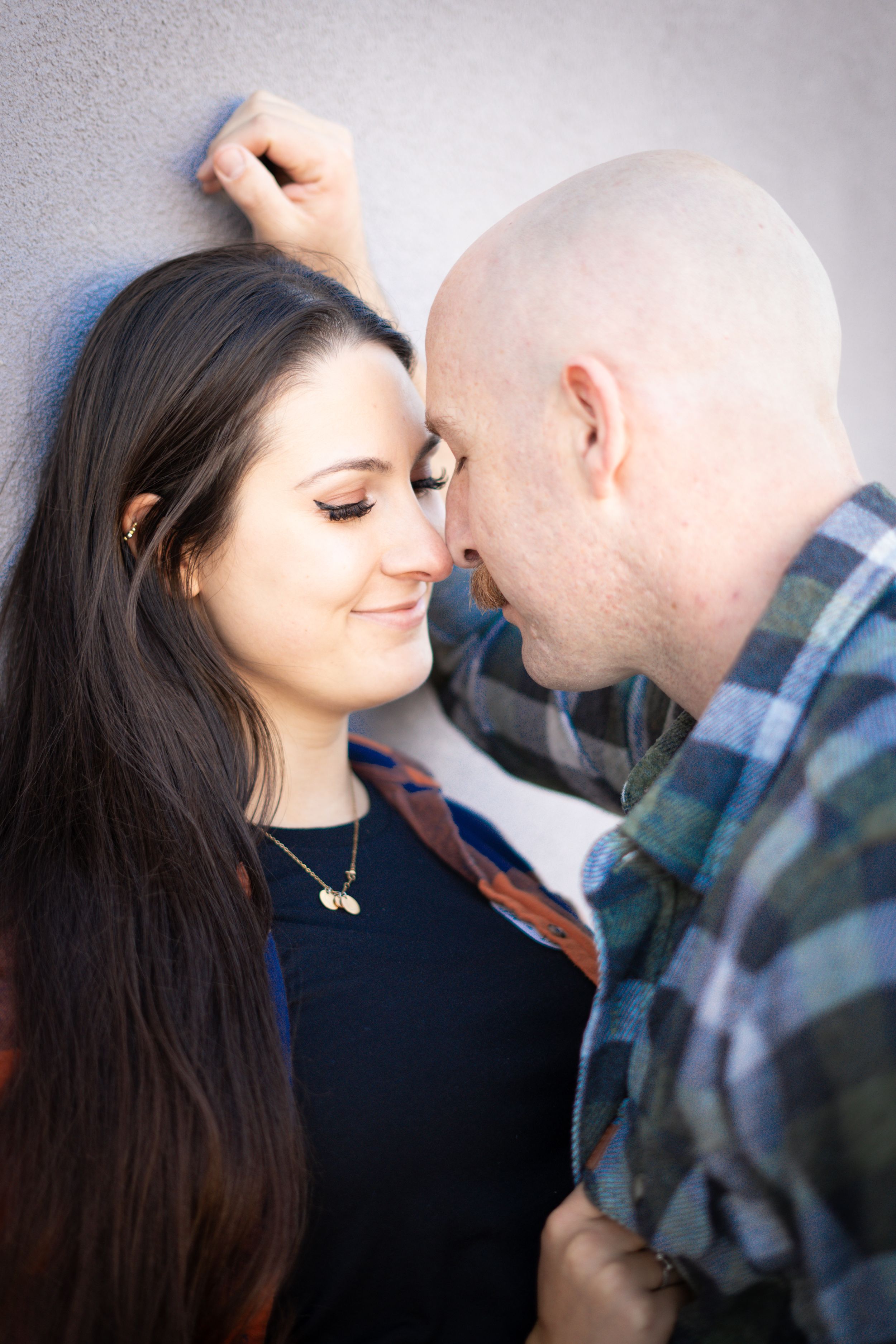 Intimate portrait of couple in casual clothing against grey wall.