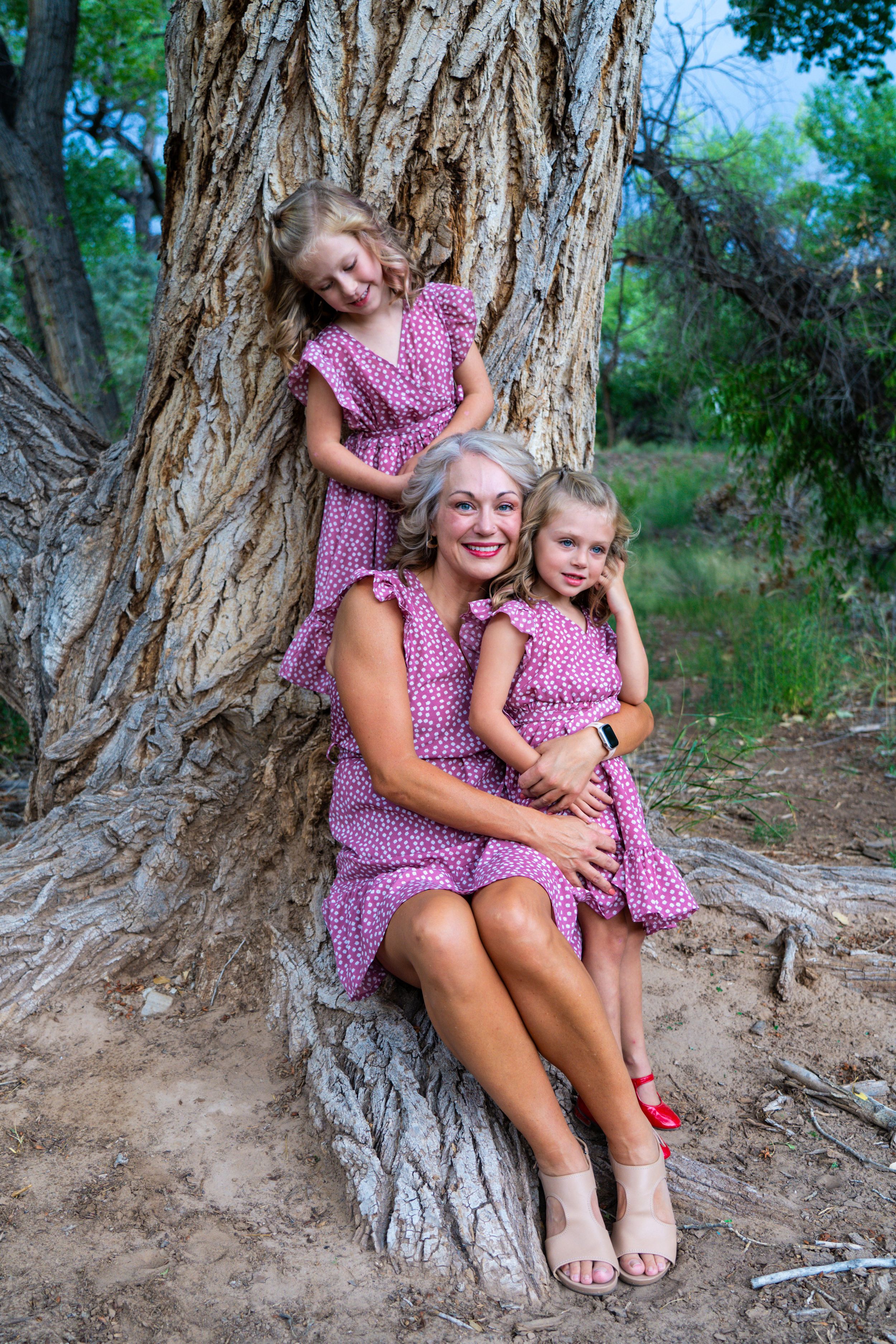 A matching pink floral print dresses photo taken against a large tree trunk in nature.