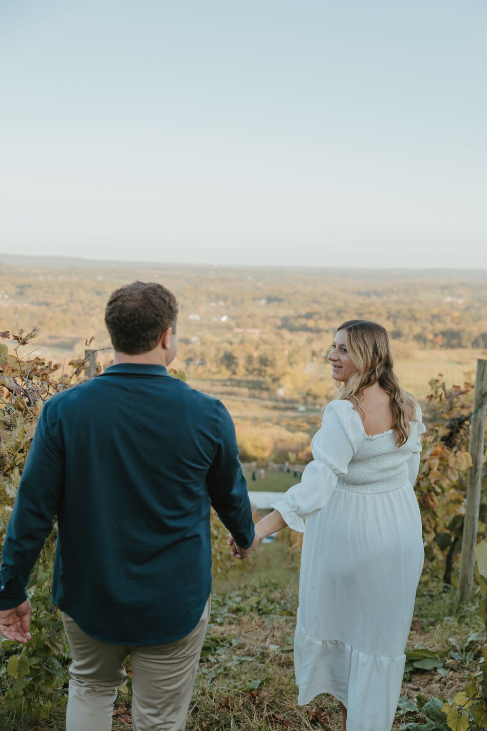 Couple enjoying scenic vineyard view while standing on hilltop at sunset.