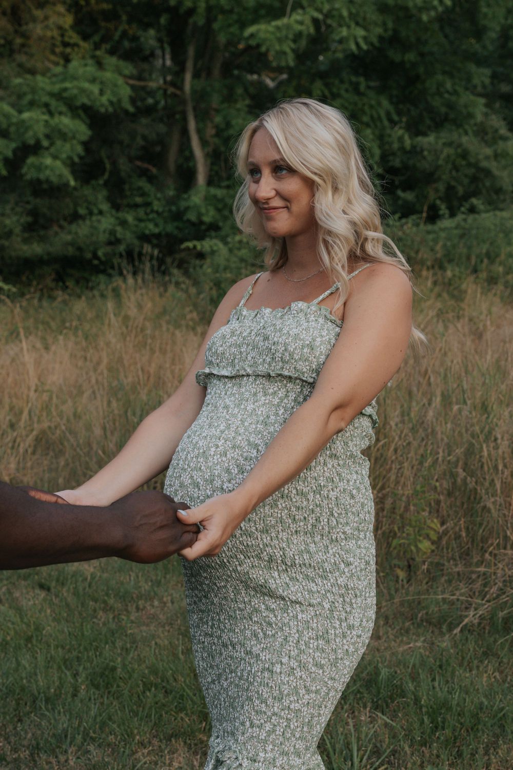 A maternity photo showing a couple holding hands in a summer meadow.