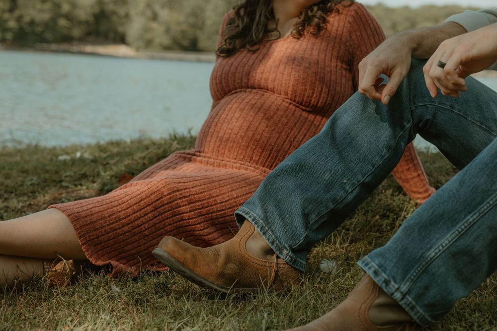 Person in orange sweater and jeans relaxing by a lake on a sunny day.