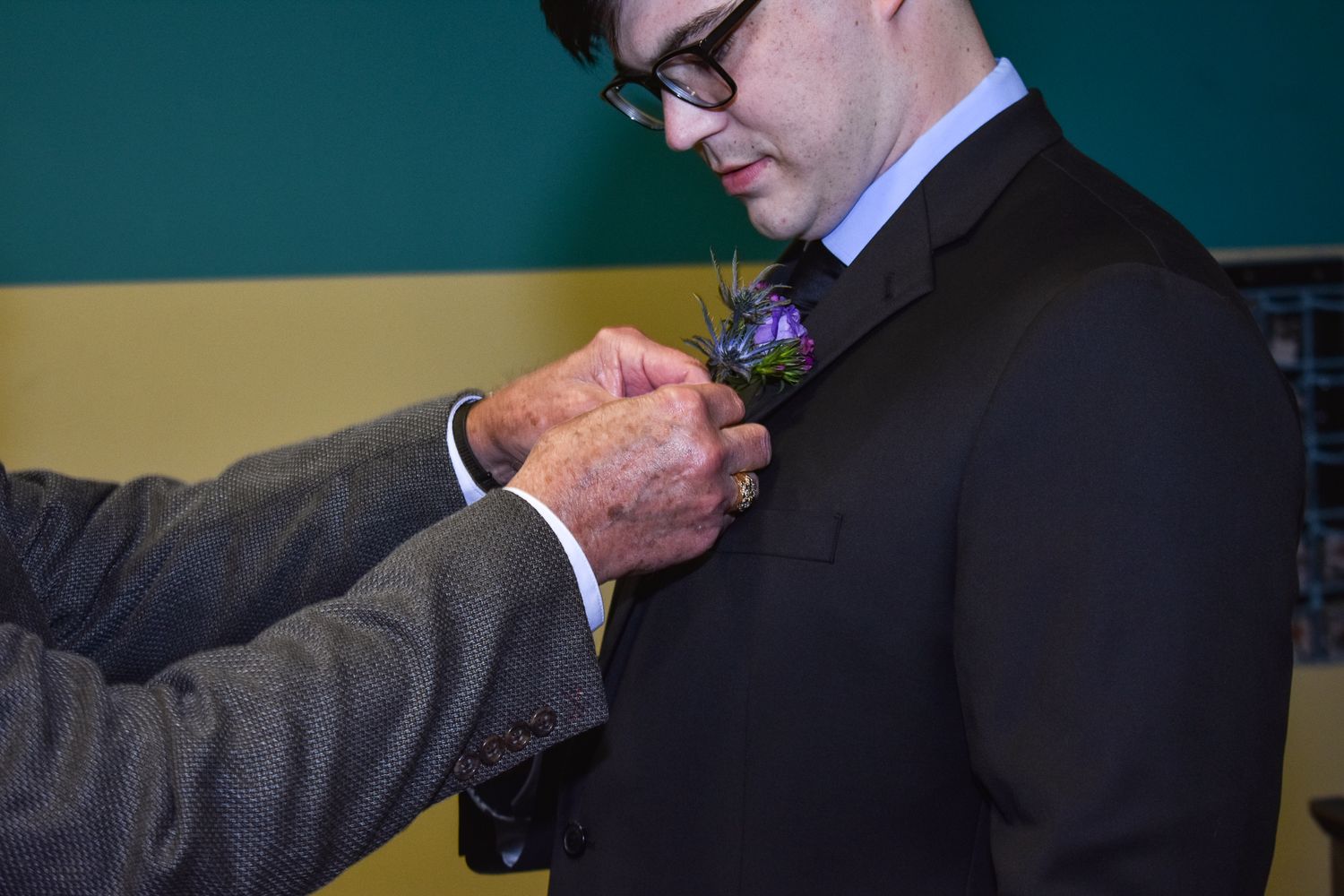 A boutonniere being pinned onto a black suit lapel during wedding preparations.