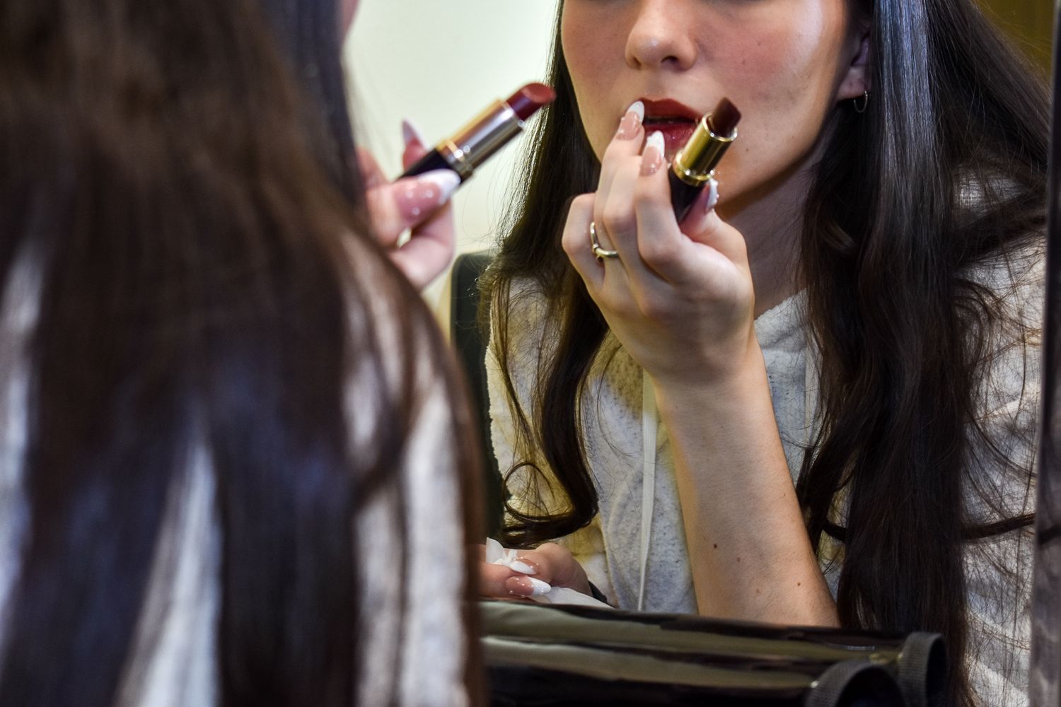 Someone applying lipstick while looking in a mirror.