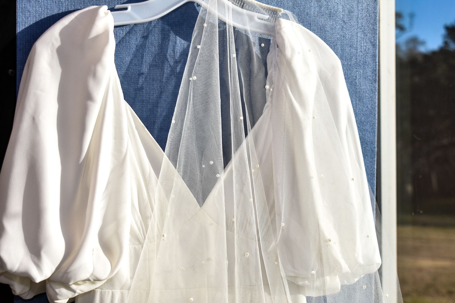 A white wedding dress with puff sleeves hanging against a blue background.