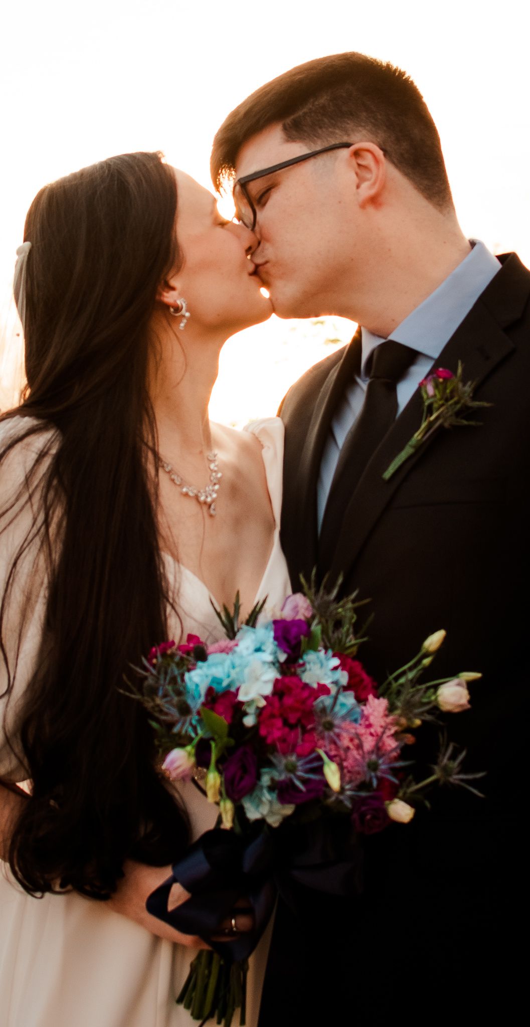 A romantic sunset portrait of newlyweds with a colorful floral bouquet.