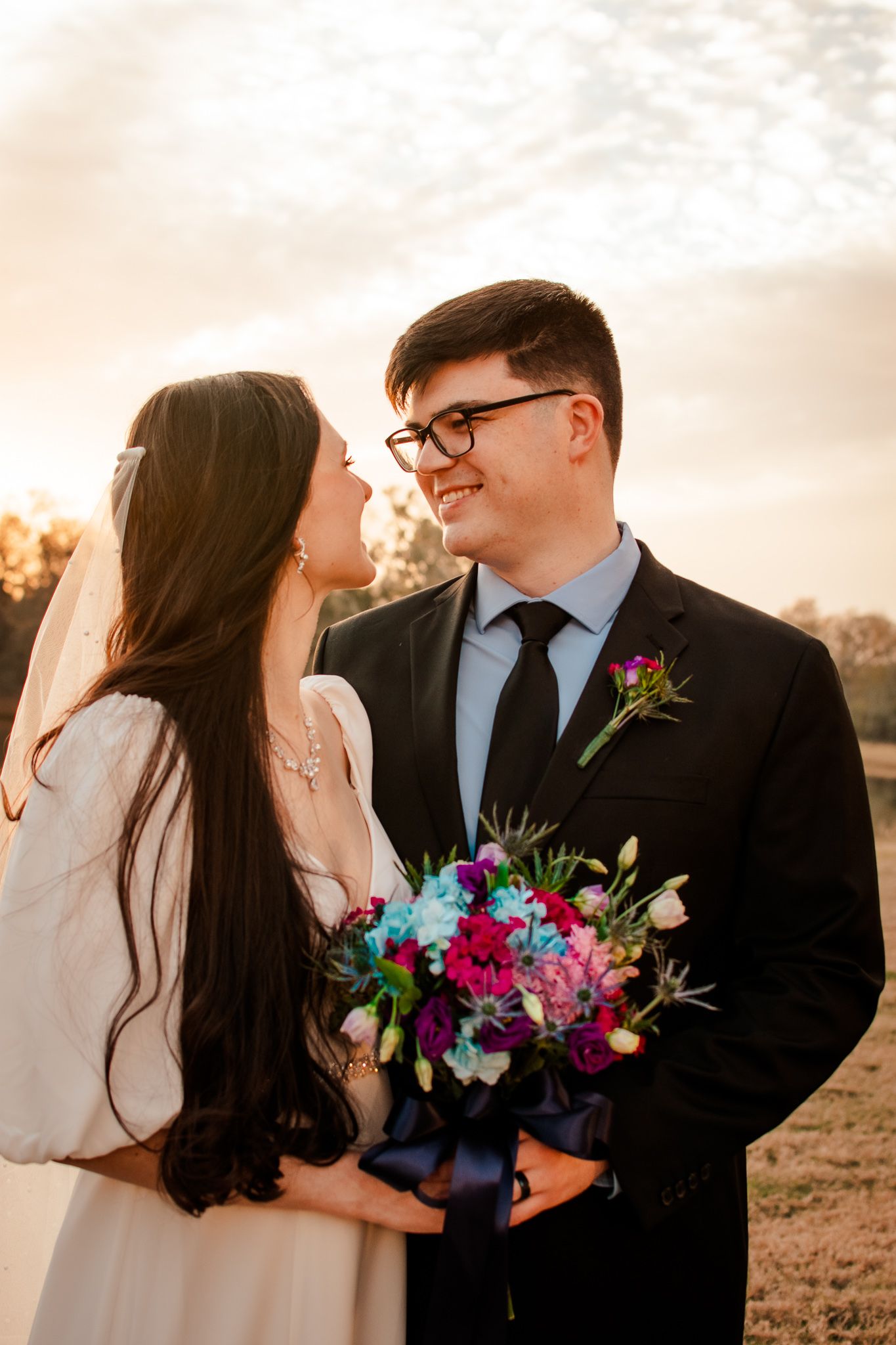A candid outdoor wedding photo capturing a loving moment at golden hour.