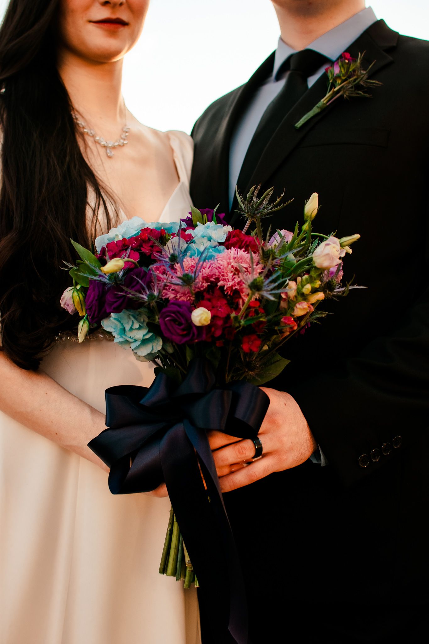 A detailed shot of a vibrant wedding bouquet with blue and pink flowers tied with a navy ribbon.