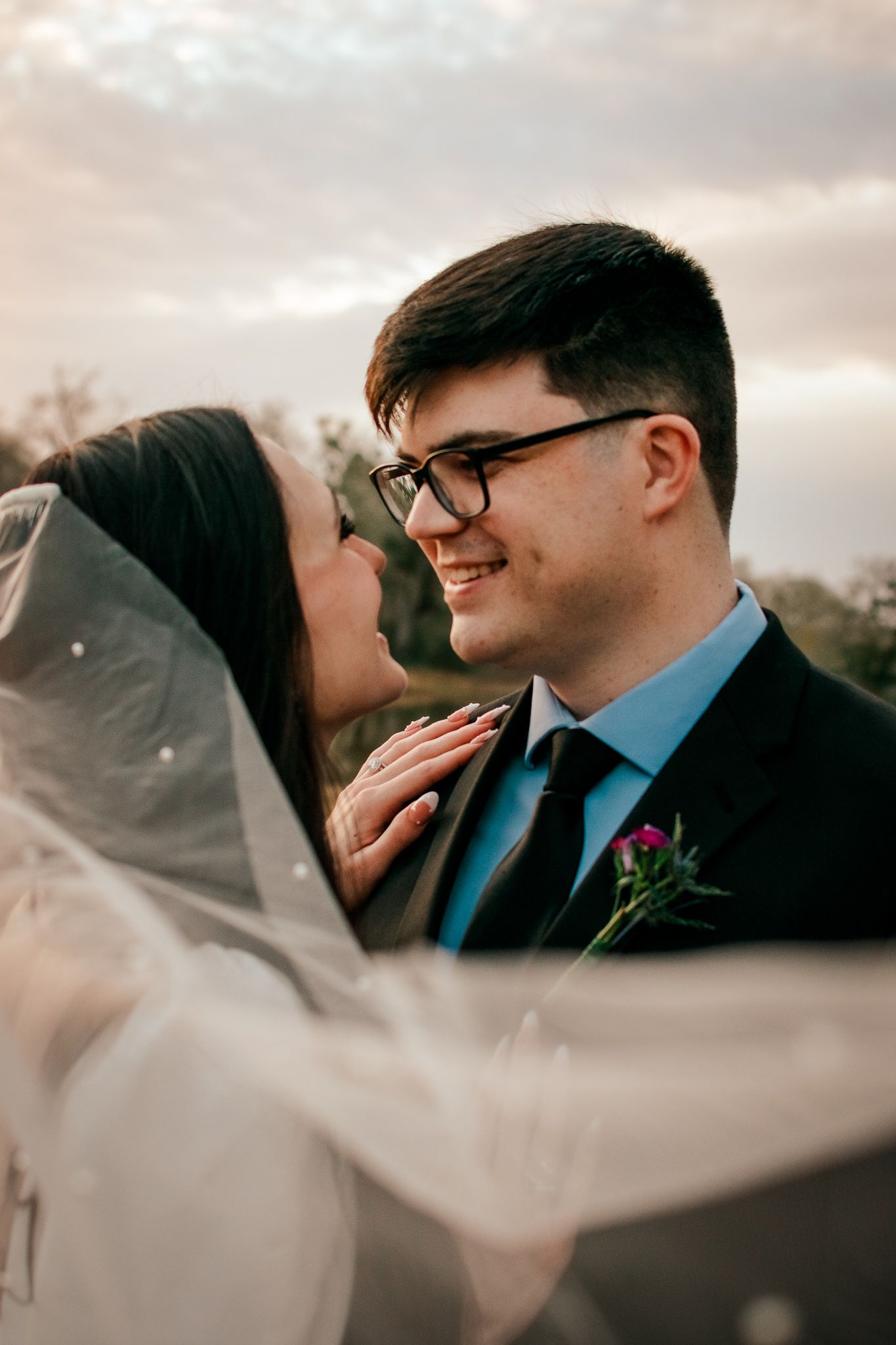 Intimate wedding moment captured during golden hour as couple shares tender embrace beneath flowing veil.
