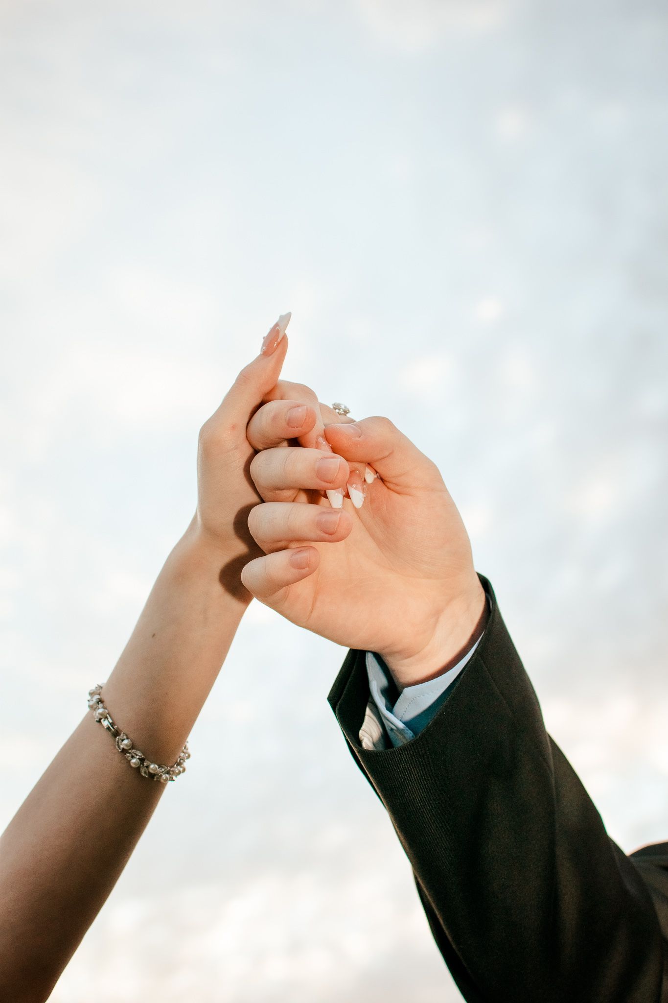 Close-up of newlyweds' hands joined against soft cloudy sky.